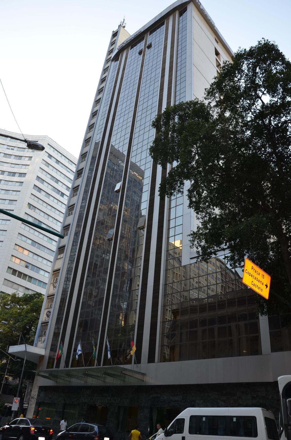 Hotel Atlantico Tower Rio de Janeiro Dış mekan fotoğraf The photo shows a city street with tall buildings. In the foreground, there is a modern glass skyscraper featuring reflective surfaces and vertical lines. Next to it, there's another building with a different architectural style, also made of glass. 